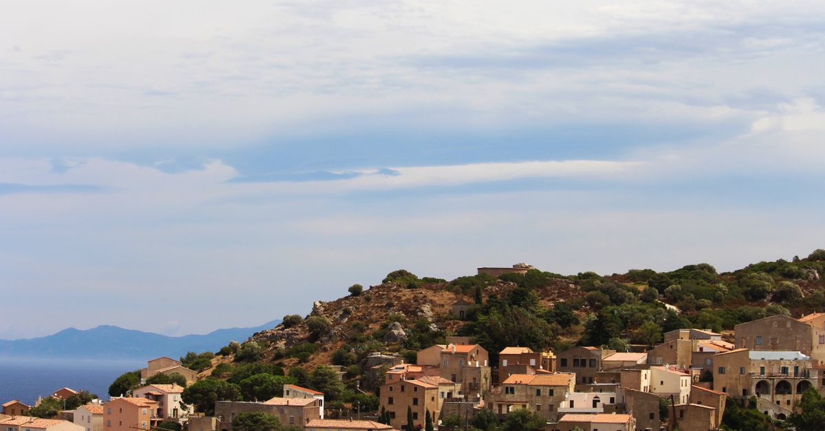 From above of small aged residential houses located on hill among green vegetation against cloudy sky in highland in nature