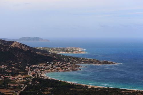 Free Drone view of coastal city located near hill on grassy coast near rippling sea against blue sky in tropical resort Stock Photo