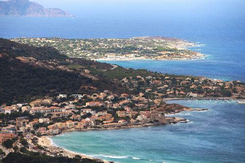 Free Drone view of town with similar houses located on grassy coast near rippling water in coastal city in nature in sunlight Stock Photo