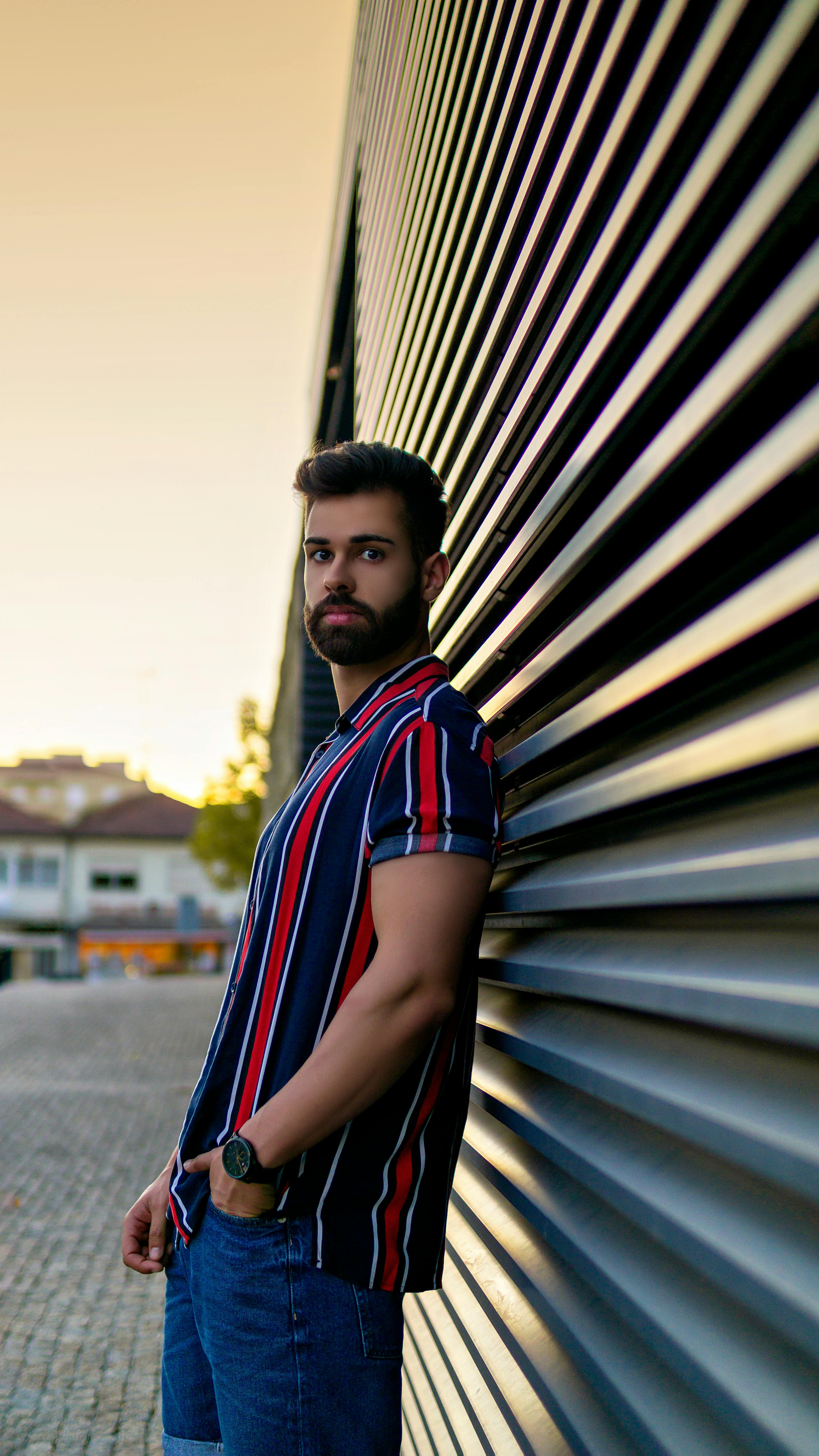 man in black white and red striped polo shirt standing near gray steel wall