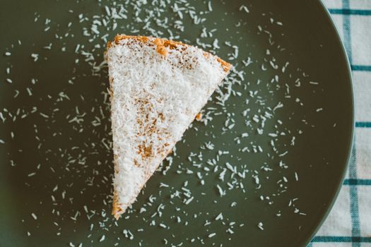 Delicious slice of cake topped with coconut flakes on a dark plate, perfect for dessert lovers.