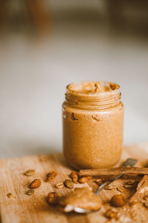 Free Close-up of a jar of creamy peanut butter on a wooden board with scattered nuts and seeds. Stock Photo
