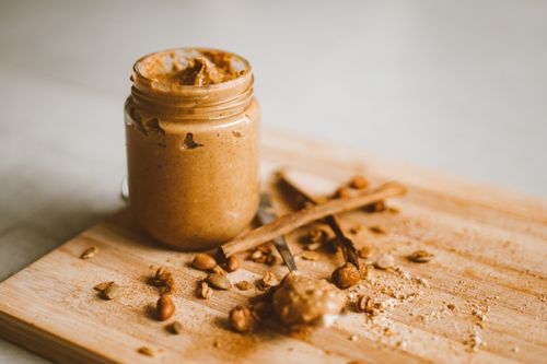 Free A jar of peanut butter with scattered peanuts and cinnamon on a cutting board. Stock Photo