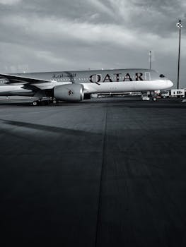 Side view of Qatar Airways airplane parked on airport tarmac under cloudy sky.