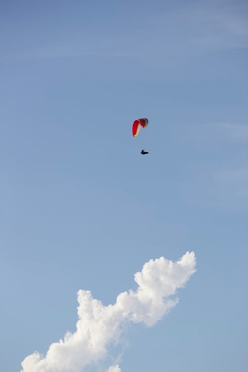 Free From below of anonymous paraglider with colorful parachute flying high in air against blue sky with clouds in sunny day Stock Photo