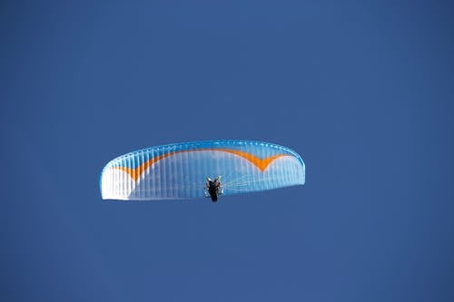 Free From below of anonymous paraglider with blue parachute flying against blue cloudless sky in nature in sunlight during practicing outside Stock Photo