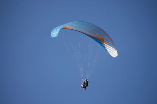 Free From below of distant unrecognizable person flying paraglider with blue parachute against blue sky in nature in sunny weather outside Stock Photo