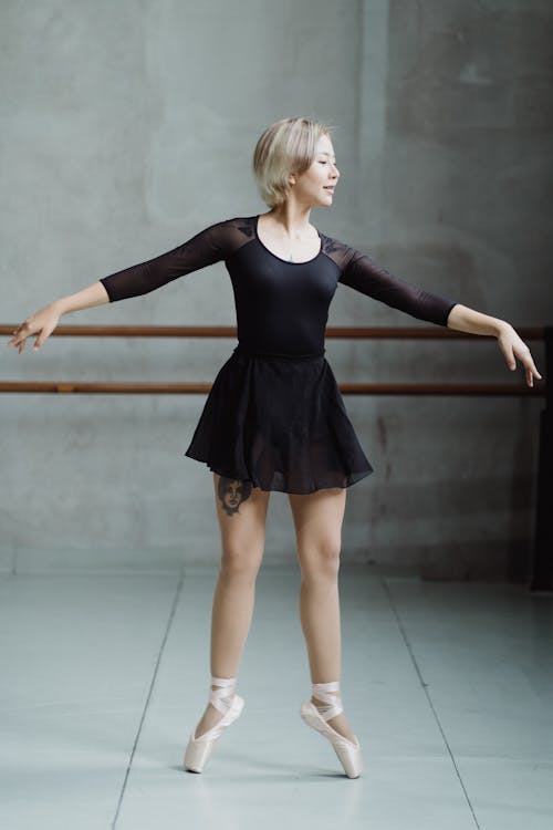 Full length graceful slim ballerina in black dress and pointe shoes standing on tiptoes and dancing in modern studio