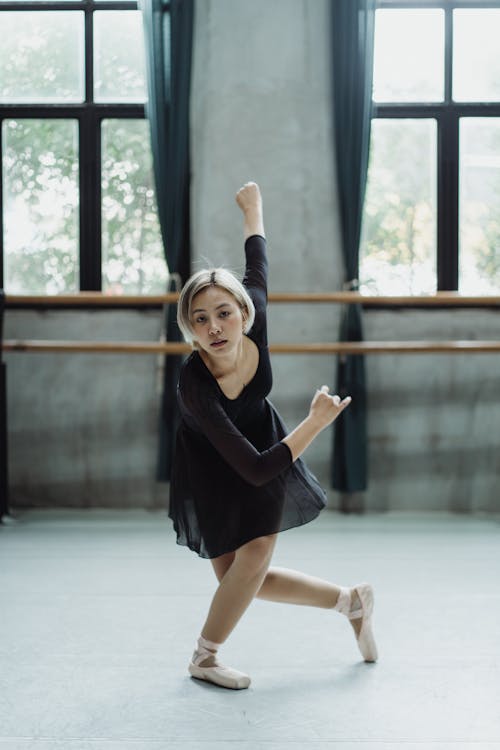 Full length of ethnic ballerina doing ballet move while rehearsing in dance studio