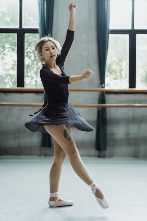 Free Full length of Asian female dancer performing graceful ballet movement while practicing skills Stock Photo