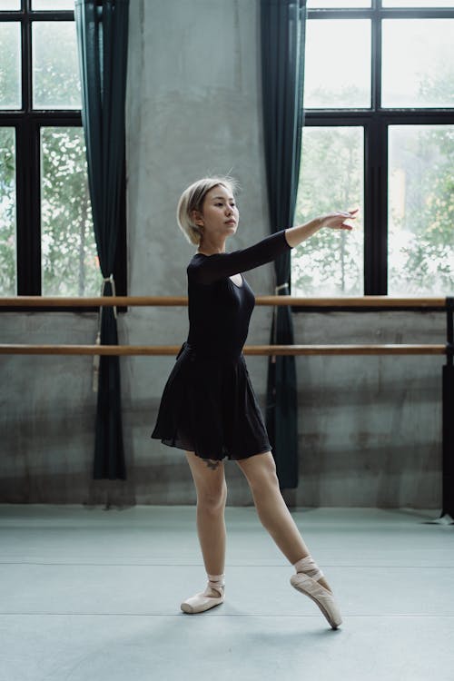 Full length of focused Asian ballet dancer performing graceful posture while practicing in studio with barre