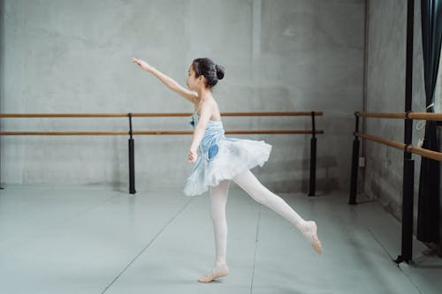 Side view full body of little ballerina practicing Arabesque position while training skills in dancing school