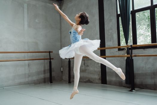 Ballerina girl performing ballet jump in studio