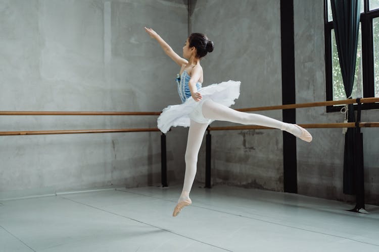 Ballerina Girl Jumping Gracefully And Dancing Ballet In Studio