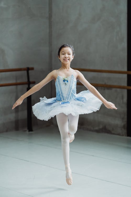 Cheerful ethnic ballerina jumping while dancing in studio
