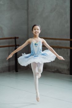 一位才华横溢的年轻芭蕾舞演员在工作室里快乐地练习芭蕾舞动作，她穿着蓝色的芭蕾舞短裙