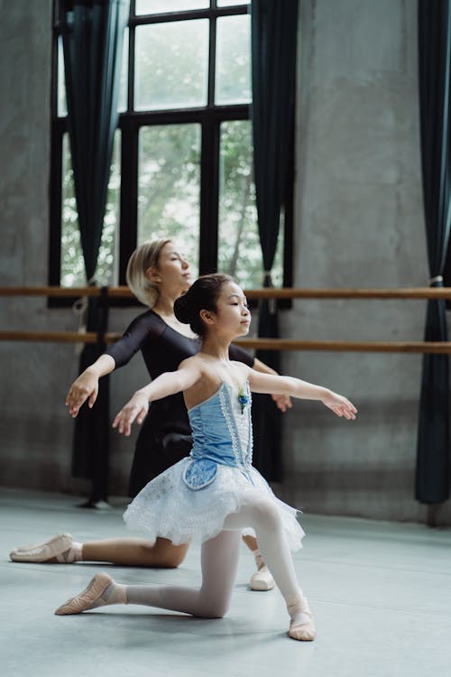 Full body side view of Asian girl repeating ballet moves with personal instructor in dance class