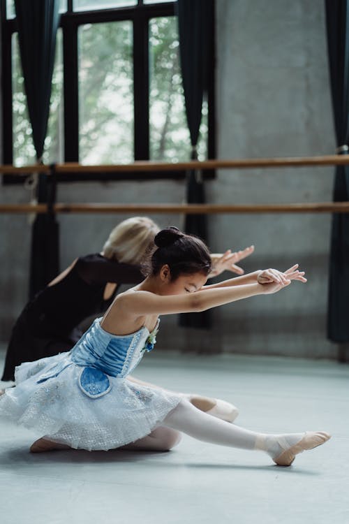 Side view full body of little girl rehearsing ballet dance with coach in studio