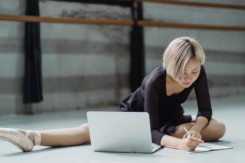 Focused Asian ballerina sitting on floor in classroom