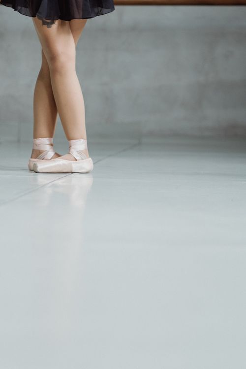 Free Anonymous female ballet dancer standing on floor in pointe shoes in studio against gray wall during rehearsal in dancing room Stock Photo