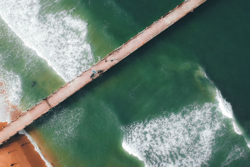 Free Top view of wavy sea with sandy coast of beach and long concrete bridge Stock Photo