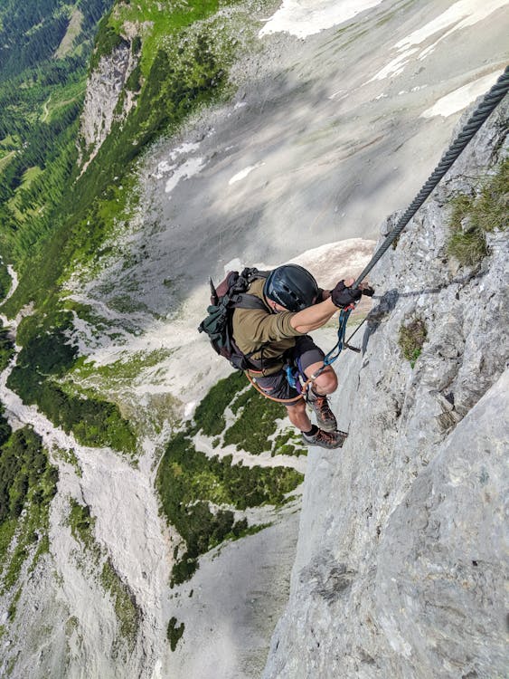 Free Man Carrying a Backpack Climbing a Mountain Cliff Stock Photo