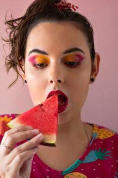 Close-up of a woman enjoying a fresh watermelon slice with colorful eye makeup.
