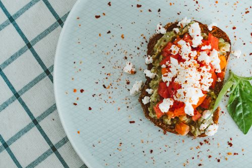 Free Top view of avocado toast with feta and tomato on a light plate with a checkered tablecloth. Stock Photo
