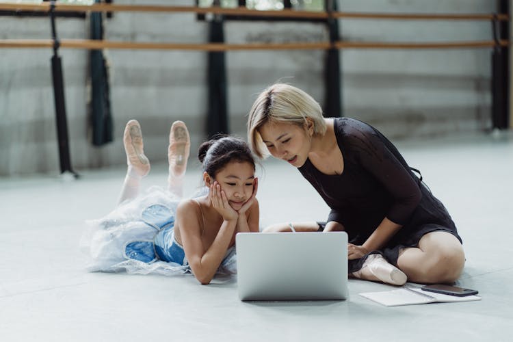 Asian Girl With Personal Instructor Using Laptop In Ballet Studio