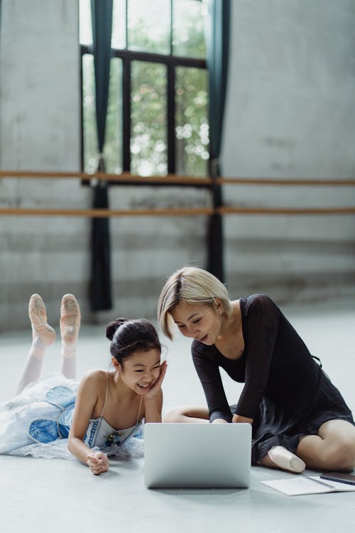 Laughing ethnic ballerina with personal instructor browsing laptop