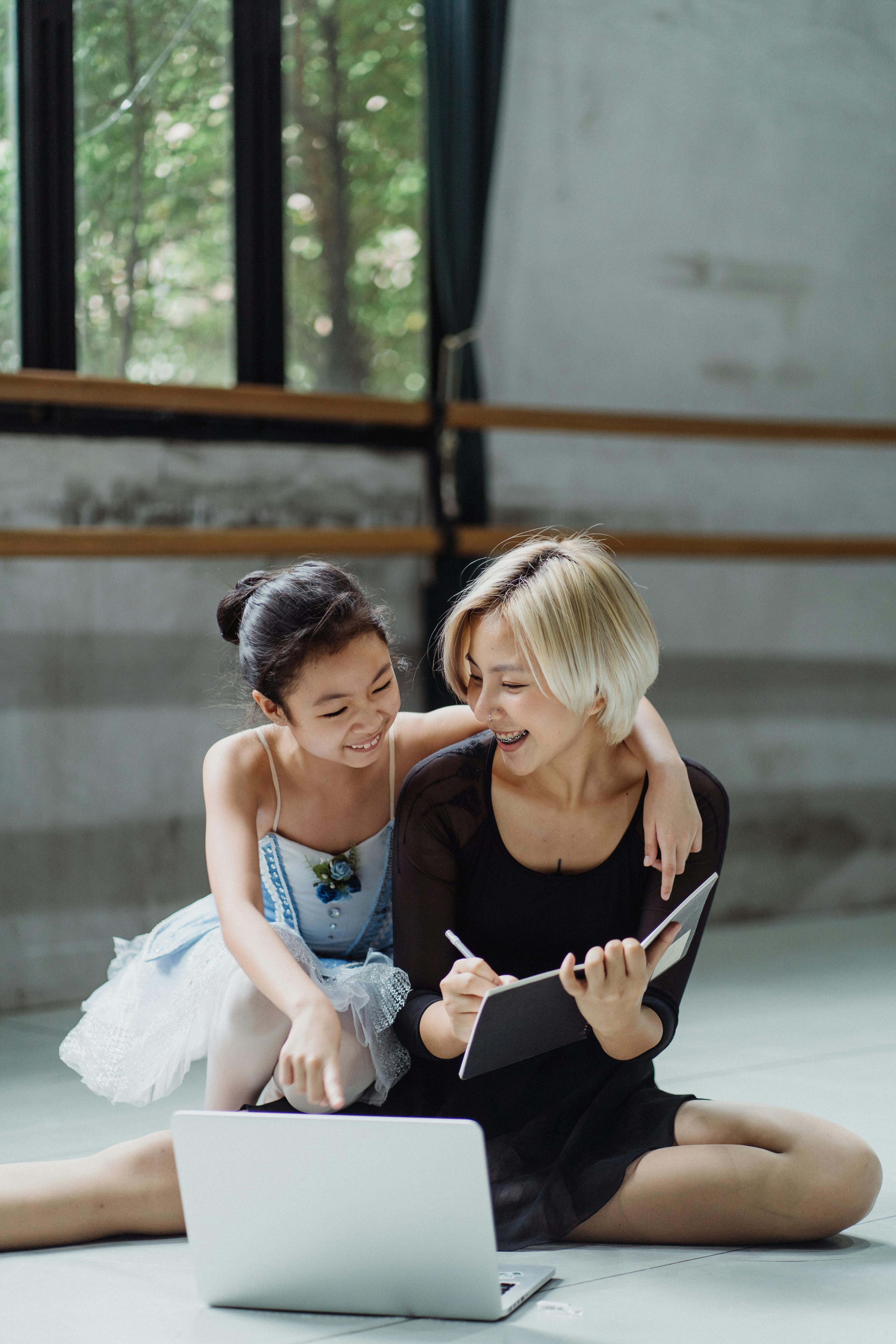 快乐的民族女孩一边指着笔记本电脑，一边在上面写下信息，同时拥抱舞蹈老师