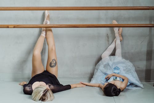 Ballet trainer holding hands with small ballerina lying on floor
