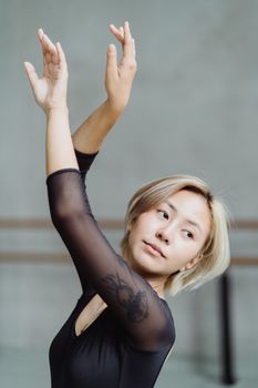 舞蹈室里，自信的亚洲芭蕾舞演员优雅地举起双手，目光移向别处