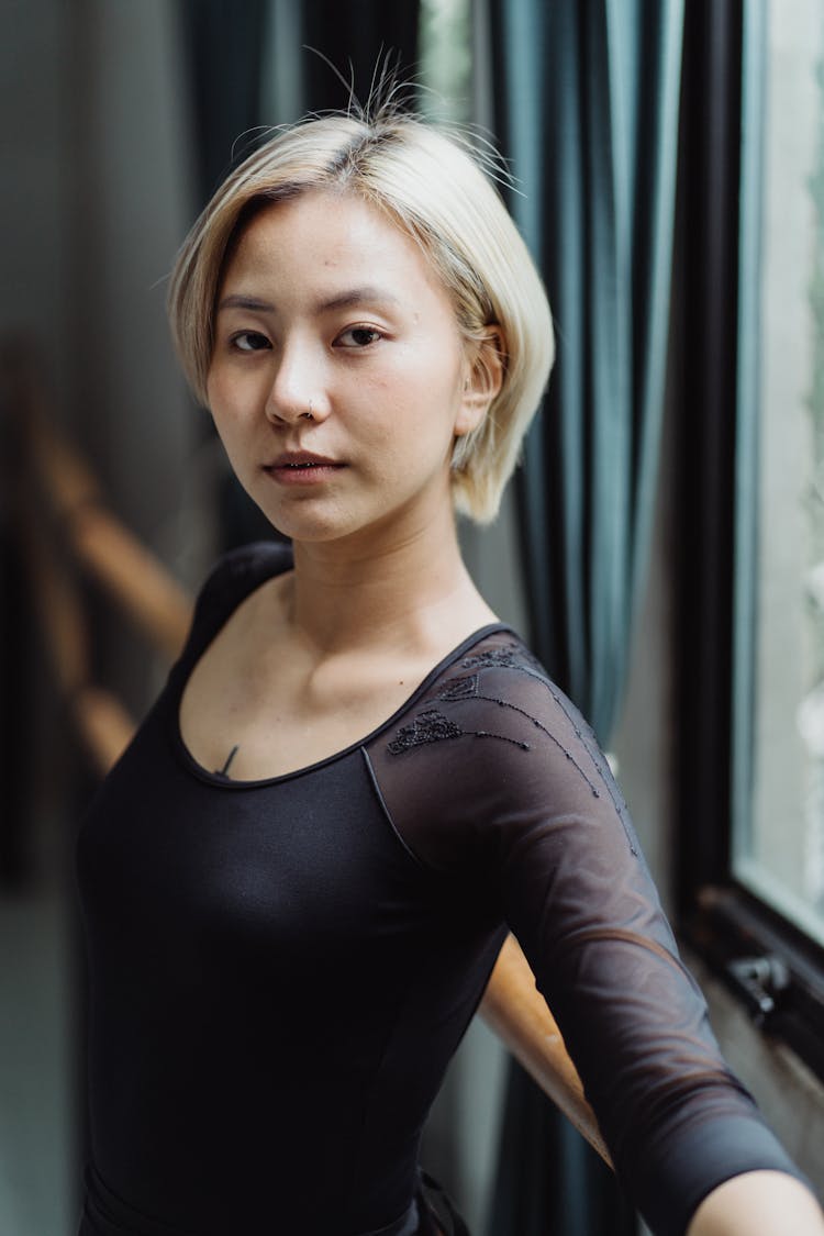 Serious Young Asian Lady Leaning On Barre In Dance Studio