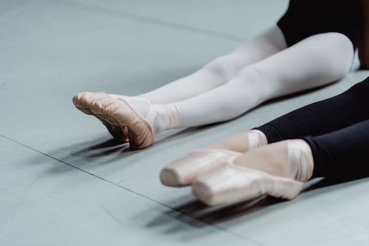 From above of crop anonymous woman and girl in pointes warming up on floor before ballet training in light studio