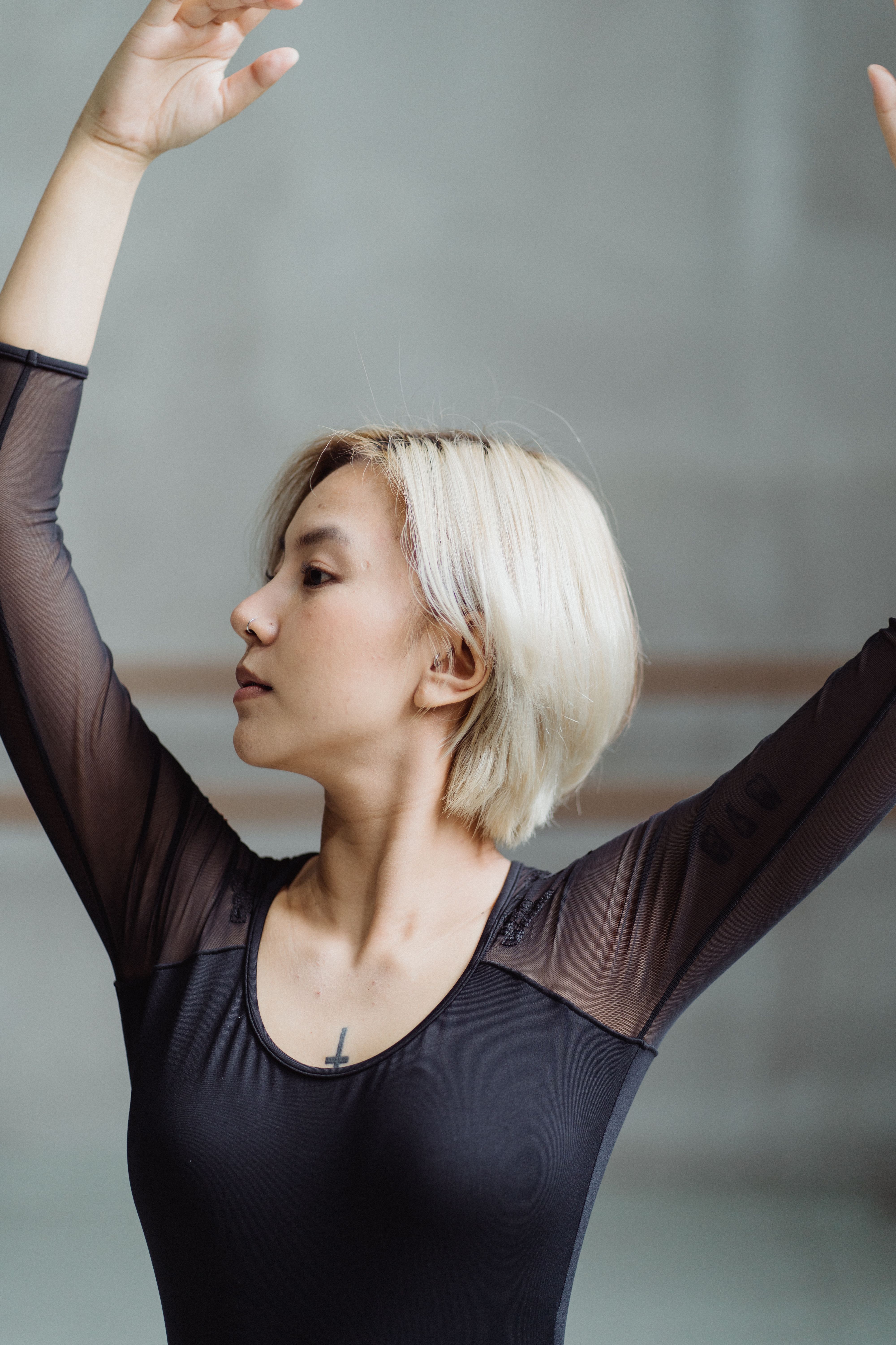 Graceful young ethnic female dancer with blond hair in black dress performing ballet movement in studio