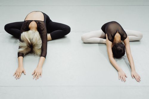 Free From above of unrecognizable young flexible ballerinas doing stretching exercise in Butterfly pose during dance class Stock Photo