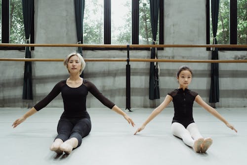 Ballet teacher with girl doing exercises together on floor in studio