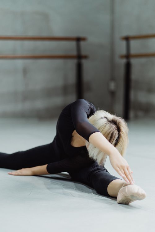 Free Flexible faceless ballerina doing twine and bending to leg of floor during rehearsal in ballet class Stock Photo