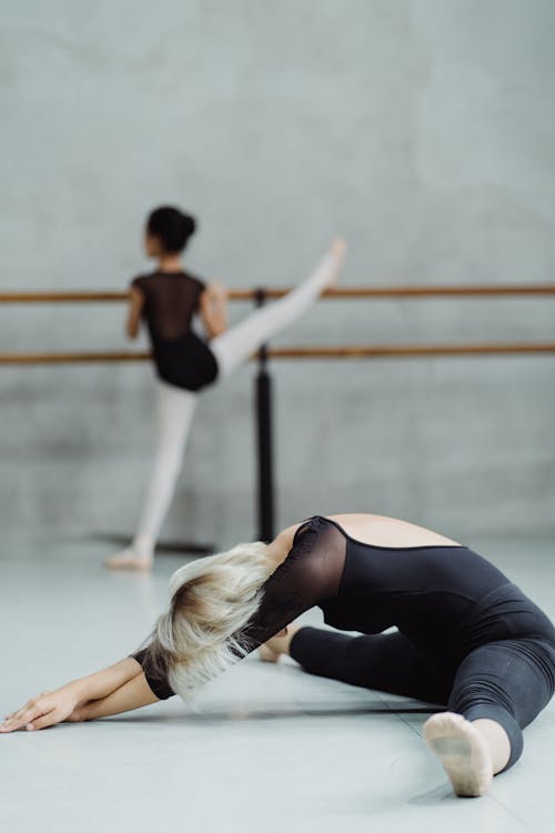 Full body of faceless ballet teacher stretching body before ballet class with pupil on barre
