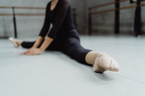 Free Faceless ballerina warming up during dance rehearsal and stretching muscles of legs in ballet hall Stock Photo
