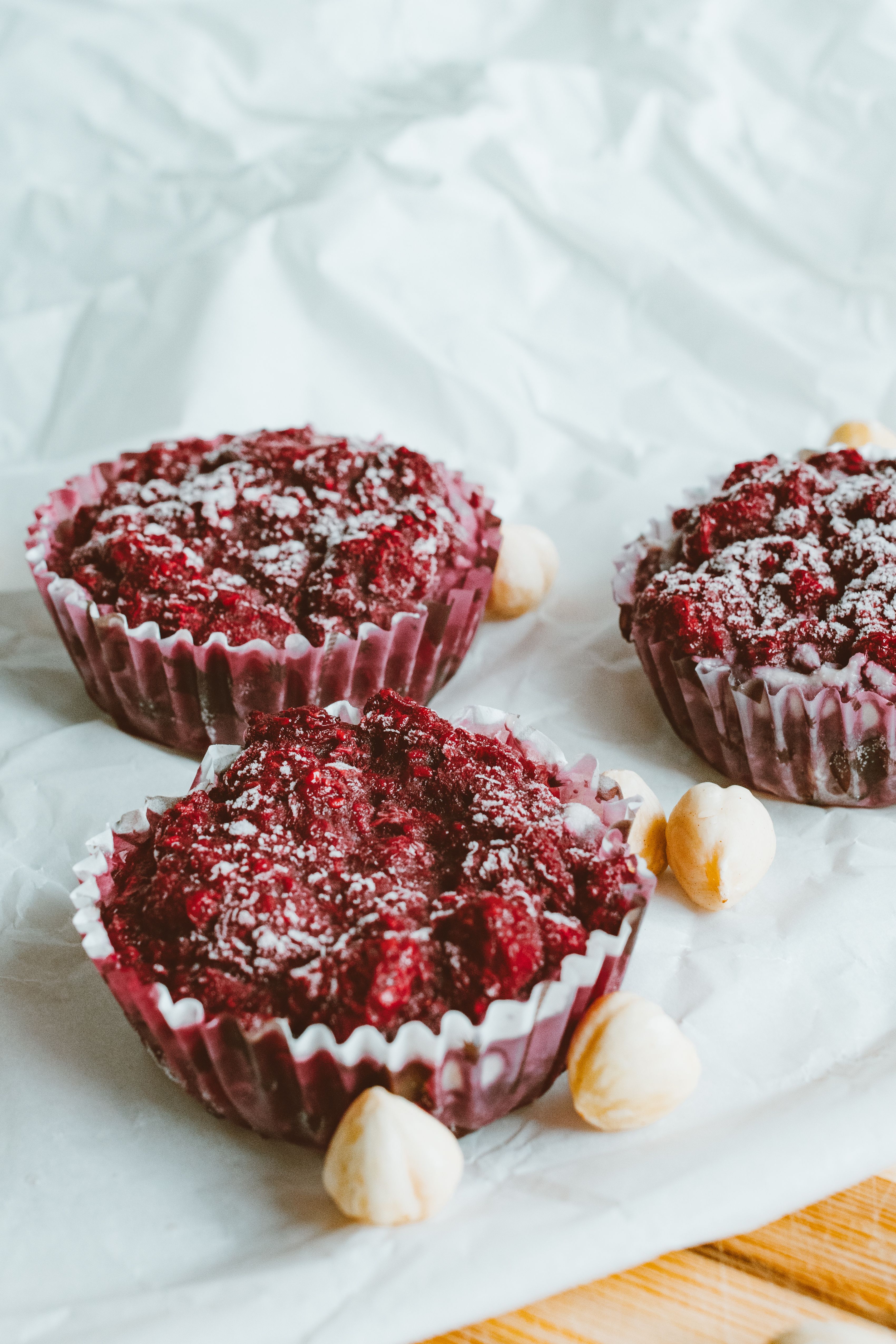 Close-up of berry muffins topped with sugar, surrounded by hazelnuts on a light background.