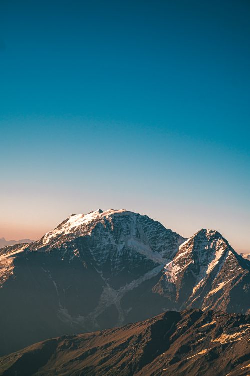 Free Stunning view of snow-capped mountains under a clear blue sky at sunrise. Stock Photo