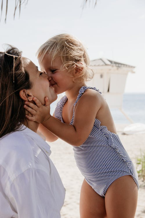 Happy little girl kissing mother on beach near sea