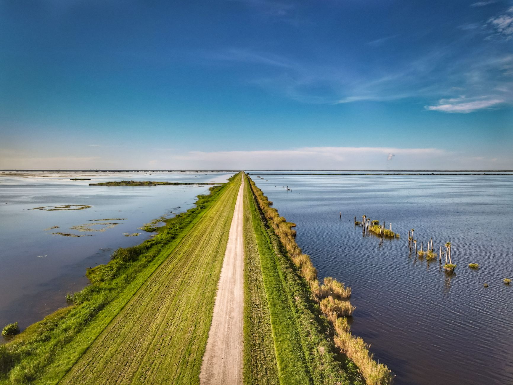 Aerial perspective of a road flanked by wetlands and open water under a clear blue sky.