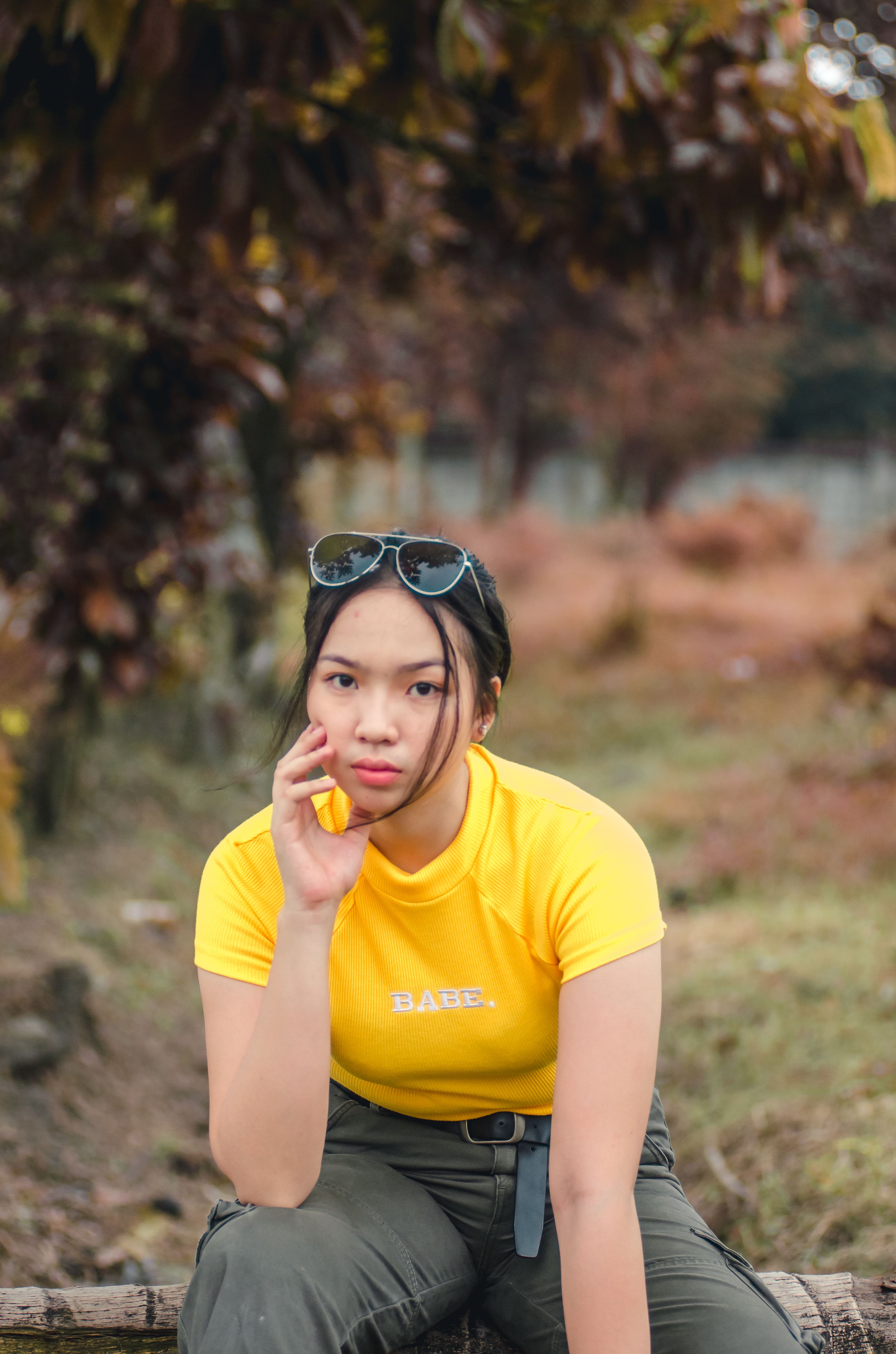 Portrait of a young woman sitting outdoors in an autumn landscape wearing a yellow t-shirt.