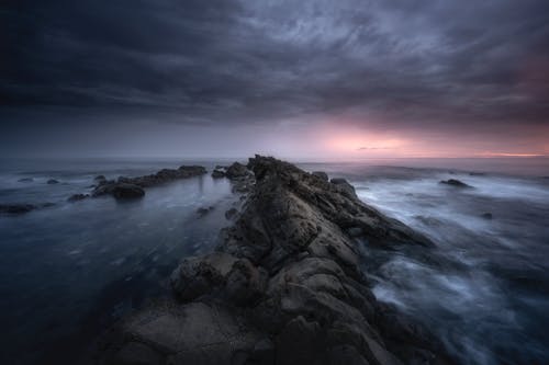 Overcast sky above boulders in sea in evening