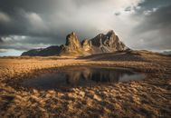 Overcast sky covered with dense clouds above small round puddles in meadow with dry yellow grass near tall steep mountain in valley