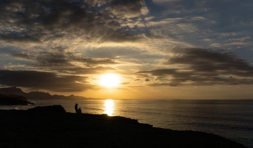 Free Silhouettes of people on the shore with a dramatic sunset and clouds over the ocean. Stock Photo