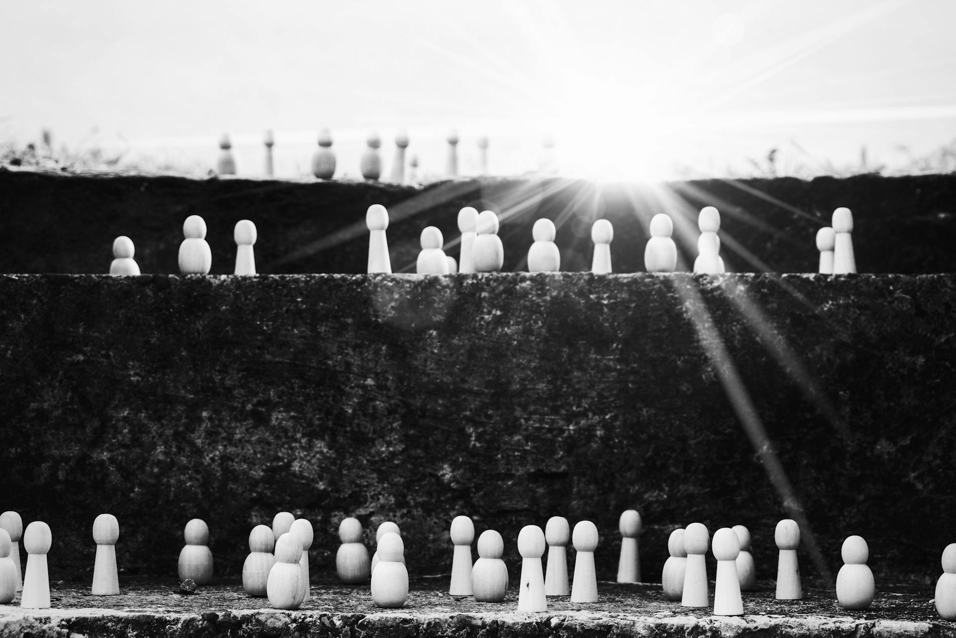 Black and white heap of wooden figurines placed on stairs illustrating social mobility and hierarchy on street with bright sunlight